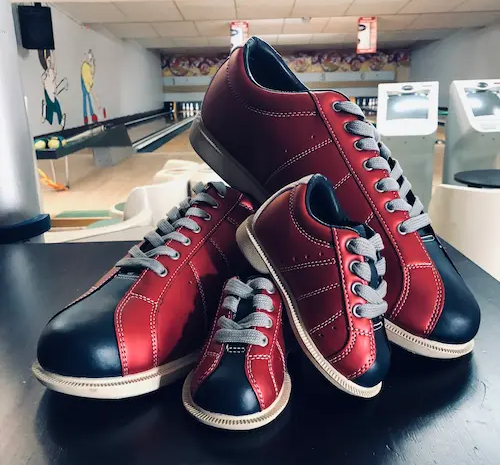 A pile of bowling shoes on a counter in front of the lanes.